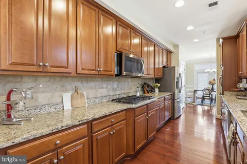 a kitchen with stainless steel appliances granite countertop wooden cabinets a sink dishwasher and a stove top oven with wooden floor