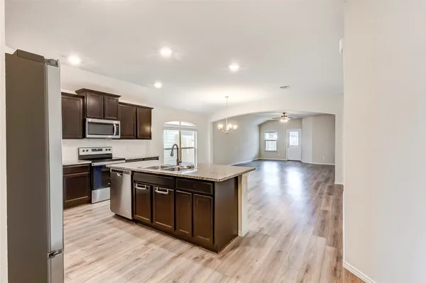 a kitchen with stainless steel appliances granite countertop a stove top oven a sink dishwasher a refrigerator and a microwave oven with wooden floor
