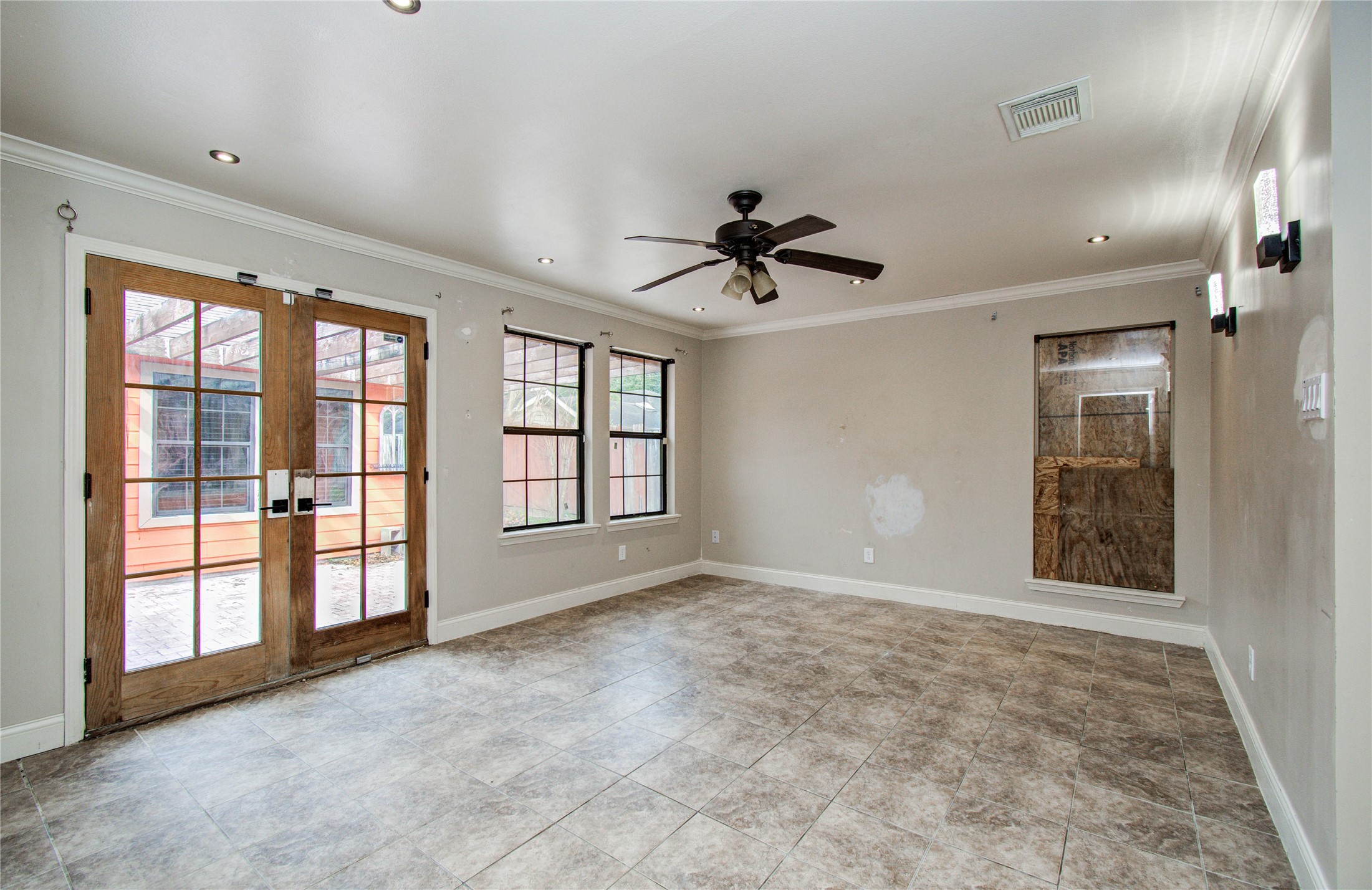 2006 Waterelm Drive Houston, TX 77084 - Photo 20 of 27 This spacious primary bedroom boasts elegant tile flooring, abundant natural light through large windows, and stylish French doors leading to a private outdoor retreat, complemented by modern recessed lighting and a ceiling fan for ultimate comfort.