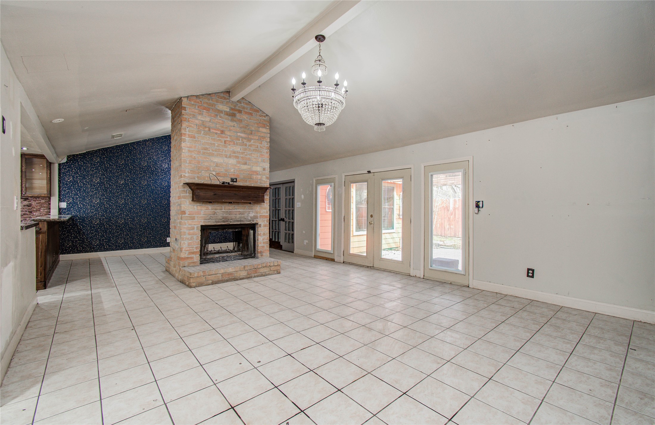 2006 Waterelm Drive Houston, TX 77084 - Photo 3 of 27 Open living room with a bold rustic brick fireplace, elegant chandelier, and abundant natural light streaming through French doors, creating a warm and inviting atmosphere perfect for relaxation and entertaining.