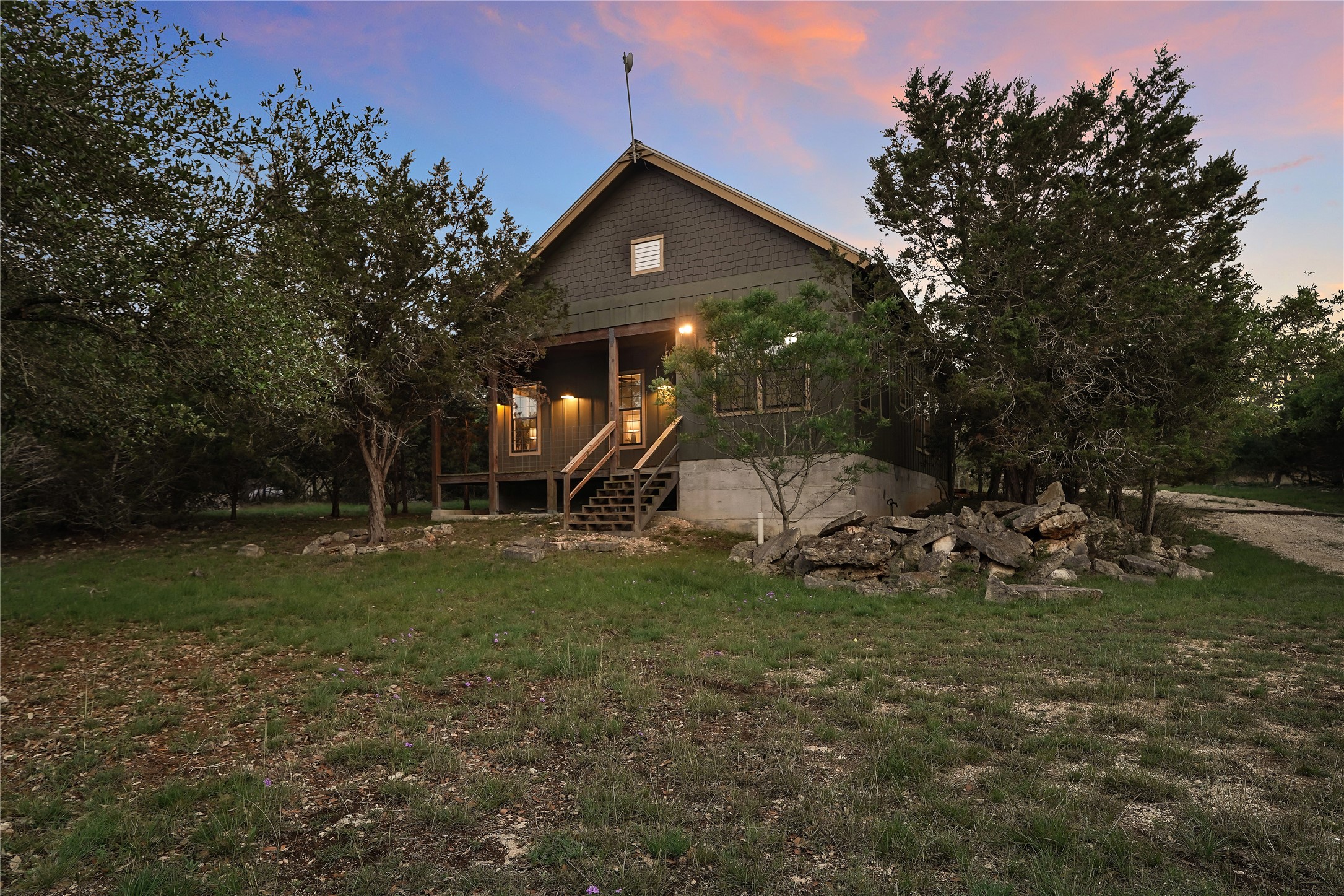 786 Beauchamp Road Dripping Springs, TX 78620 - Photo 28 of 40 The property features a dark gray exterior, a covered porch with a wooden staircase, and ample surrounding greenery