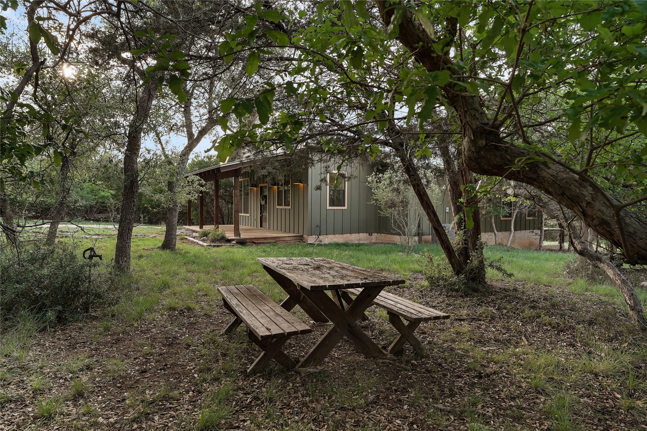 786 Beauchamp Road Dripping Springs, TX 78620 - Photo 36 of 40 The property features a natural setting with mature trees and a wooden picnic table, complemented by a covered porch with wooden decking