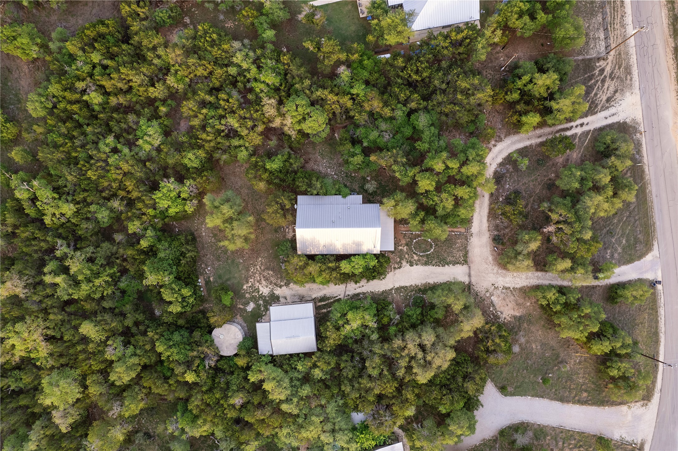 786 Beauchamp Road Dripping Springs, TX 78620 - Photo 38 of 40 This property features a main building with a gray metal roof, a smaller auxiliary building with a gray metal roof, and a water tank