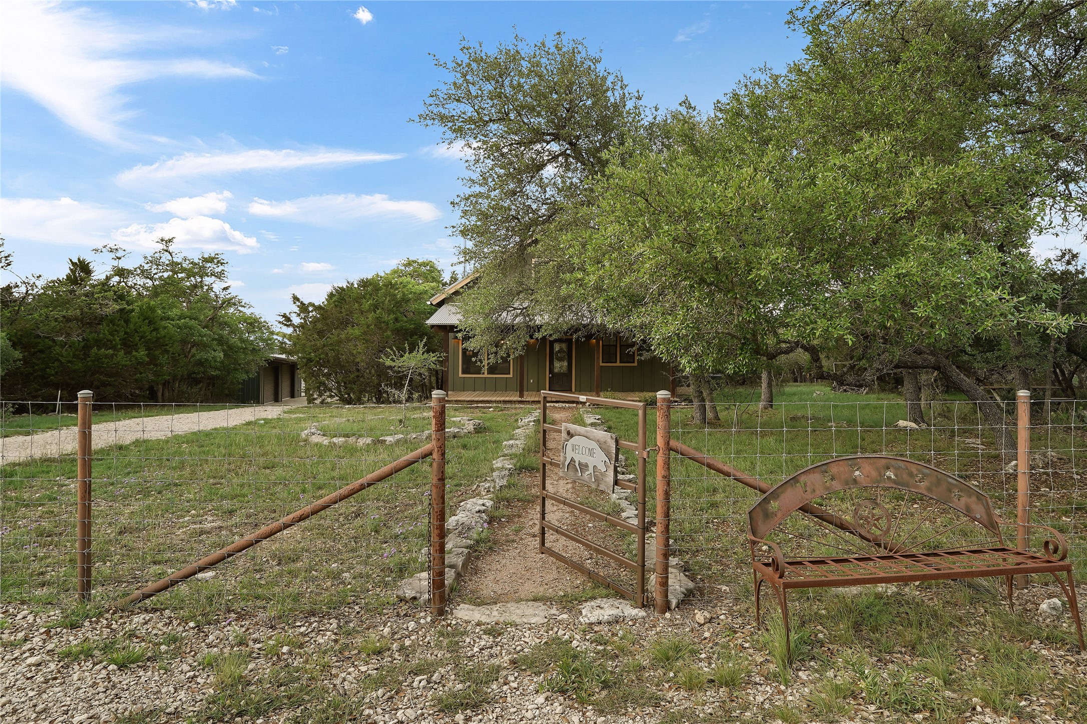 786 Beauchamp Road Dripping Springs, TX 78620 - Photo 4 of 40 The property features a green exterior and is surrounded by mature trees, a gravel pathway, and a wire fence