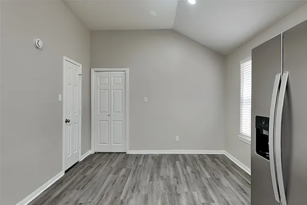 a view of an empty room with wooden floor and a refrigerator
