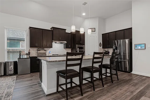 a open kitchen with stainless steel appliances kitchen island granite countertop a refrigerator a stove a sink a dining table and chairs with wooden floor