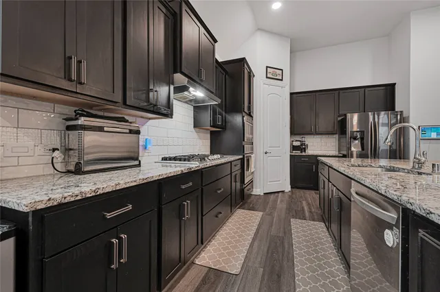 a kitchen with stainless steel appliances kitchen island granite countertop a refrigerator a stove a microwave and island with wooden floor