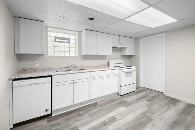 a kitchen with granite countertop white cabinets white appliances a sink and a window