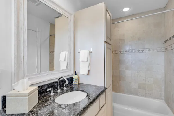 a bathroom with a granite countertop sink a mirror a bathtub and shower