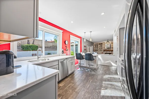 a living room with stainless steel appliances kitchen island granite countertop a refrigerator a sink dishwasher a dining table and chairs with wooden floor