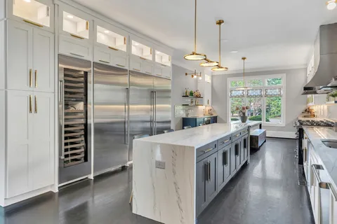 a kitchen with kitchen island a counter top space a stove a refrigerator a chimney a sink and cabinets