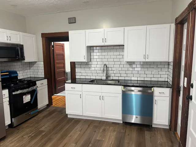 a kitchen with stainless steel appliances white cabinets a sink a stove a microwave and wooden floors