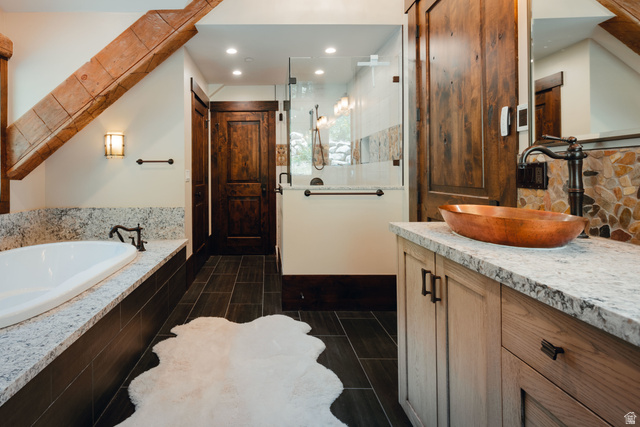 1667 West Tollgate Cyn Road Coalville, UT 84017 - Photo 30 of 61 Bathroom featuring a full-size soaking tub with a stone-finish surround, a frameless glass shower enclosure, a vanity with a copper vessel sink and stone countertop, wood-finish flooring, and exposed ceiling beams