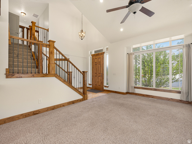 1279 West 1500th Street North Mapleton, UT 84664 - Photo 10 of 83 Living area with vaulted ceiling, large picture windows, wood-finish trim, and a prominent staircase featuring wood-finish railings and wrought iron spindles