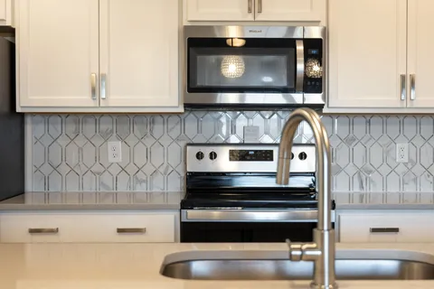 a large white kitchen with a large island oven a stove a sink a dining table and chairs with wooden floor