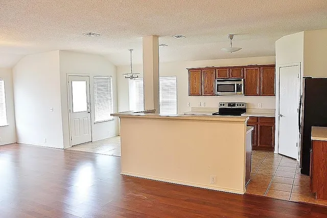 a living room with stainless steel appliances kitchen island granite countertop a refrigerator a stove a sink and a microwave with wooden floor