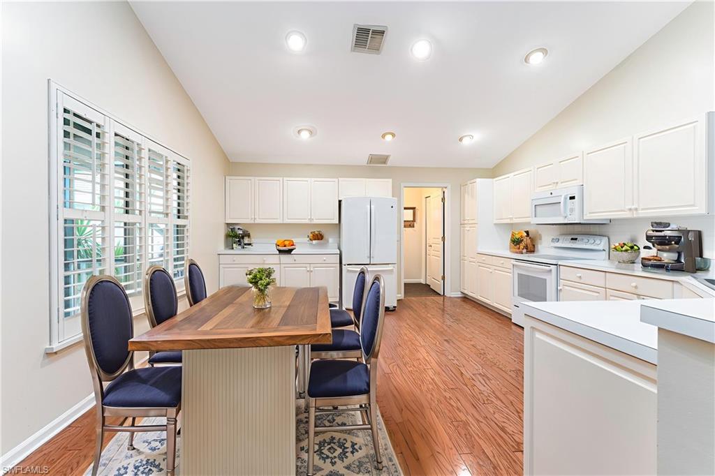 3988 Reflection Court Naples, FL 34109 - Photo 13 of 50 Kitchen with white appliances, lofted ceiling, a kitchen breakfast bar, light wood-style floors, and white cabinets