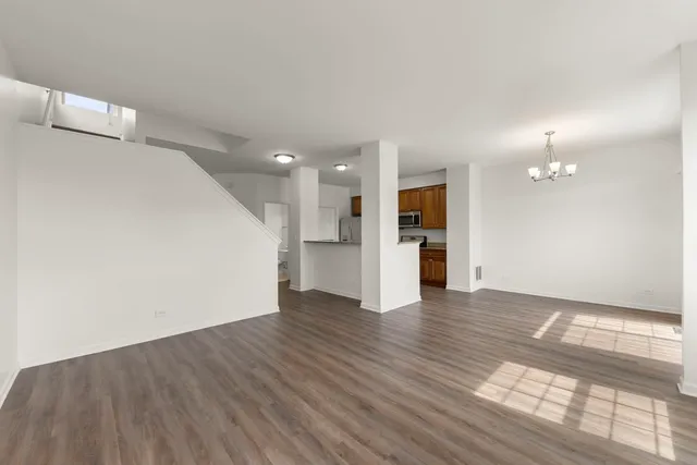 a view of an empty room with wooden floor and a kitchen