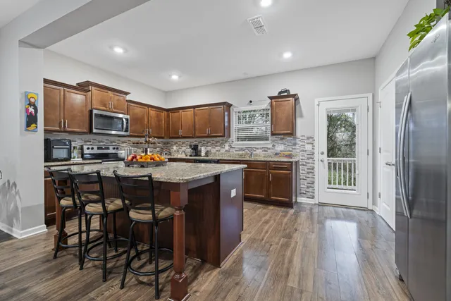 a kitchen with stainless steel appliances granite countertop wooden cabinets a refrigerator a stove a sink and a oven with wooden floor