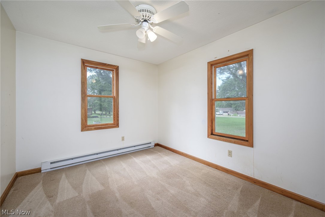 6503 Garrett Road Ravenna, OH 44266 - Photo 11 of 50 Neutral-toned carpeting, two windows with wood trim, ceiling fan, and baseboard heating unit
