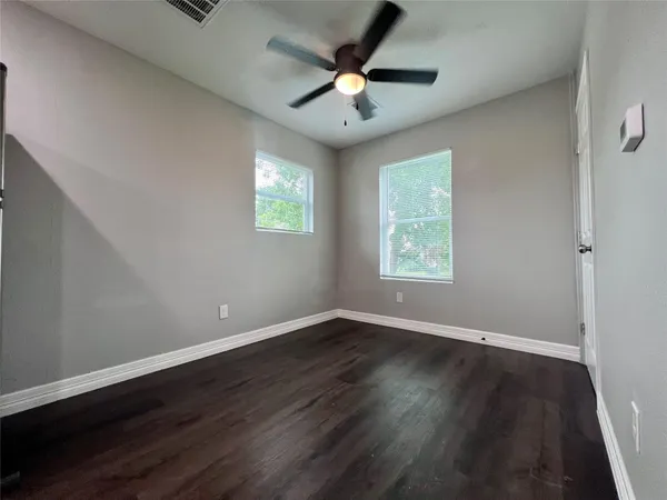 an empty room with wooden floor chandelier fan and windows