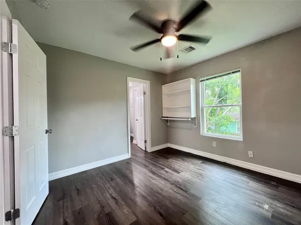 an empty room with wooden floor chandelier fan and windows