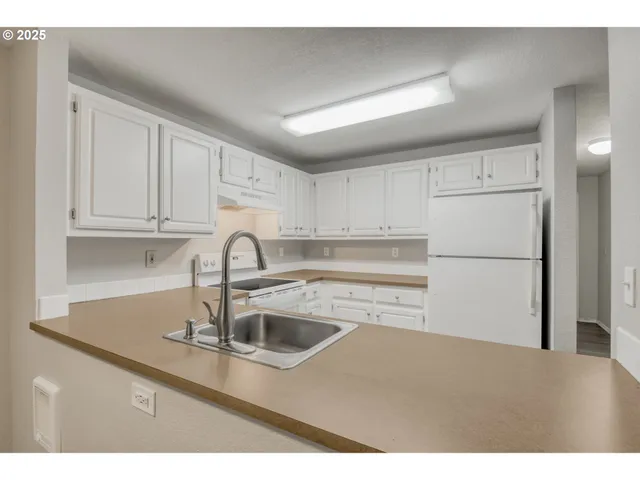 a kitchen with stainless steel appliances granite countertop a sink dishwasher a refrigerator and white cabinets with wooden floor