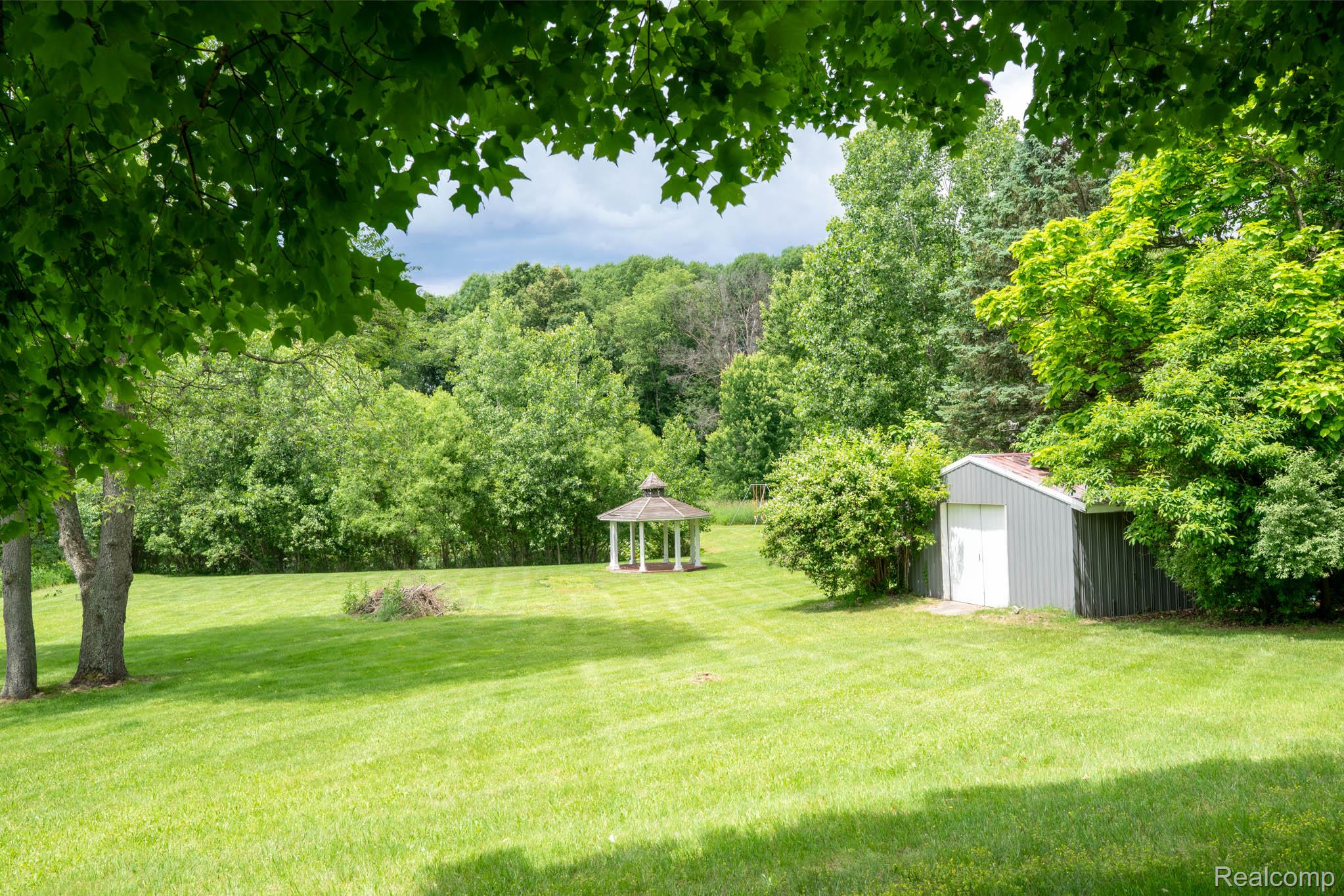 7333 Toma Road Dexter, MI 48130 - Photo 13 of 45 Expansive green lawn featuring a white gazebo, mature trees, and a gray utility shed with white doors