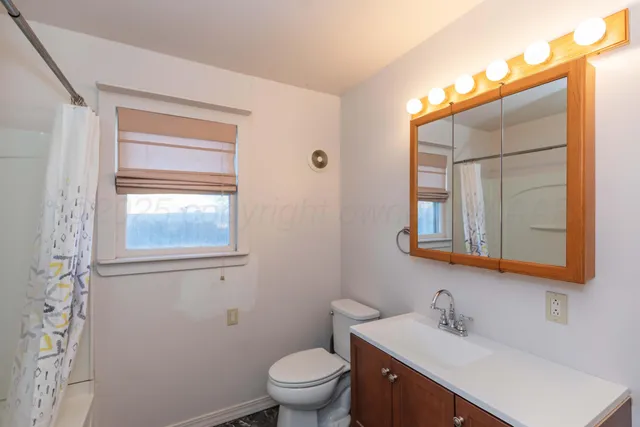 a bathroom with a toilet a sink a mirror a window and vanity