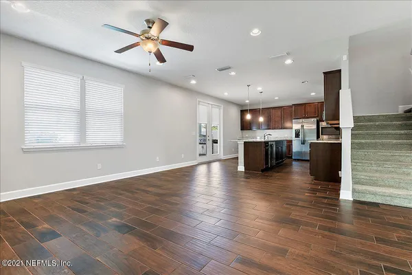 an empty room with wooden floor kitchen view and a window
