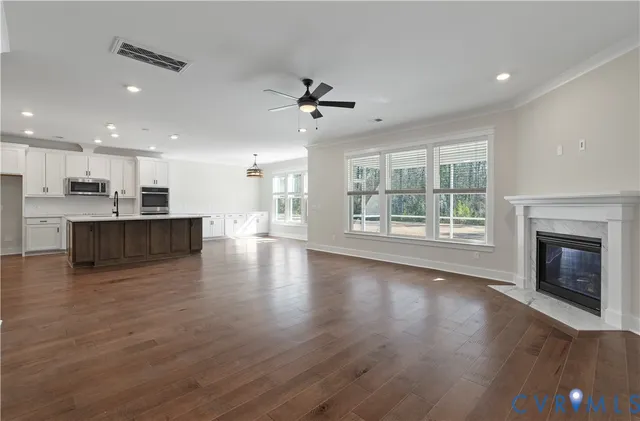 an empty room with wooden floor kitchen view and a fireplace