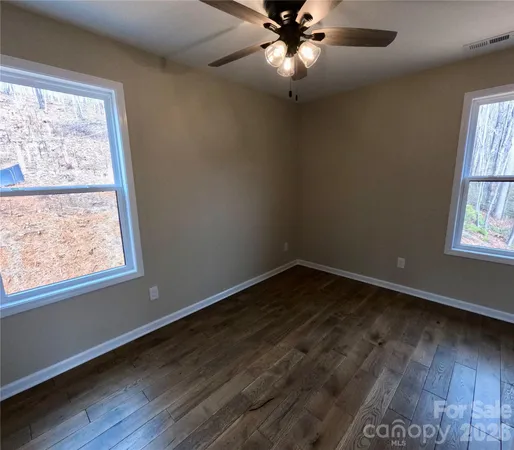 an empty room with wooden floor fan and windows