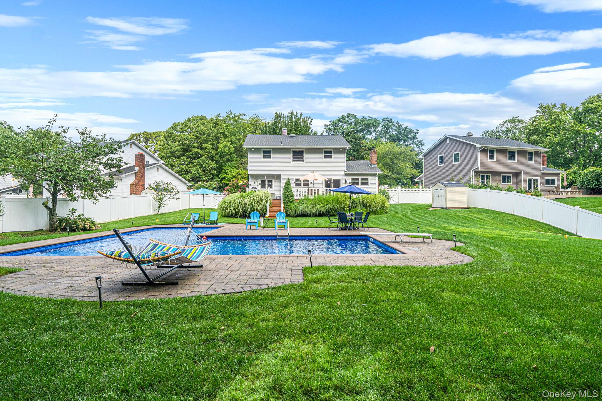 5 Rockhill Road Rocky Point, NY 11778 - Photo 42 of 48 Expansive backyard featuring an in-ground swimming pool with stone paver surround, a white privacy fence, and a detached storage shed