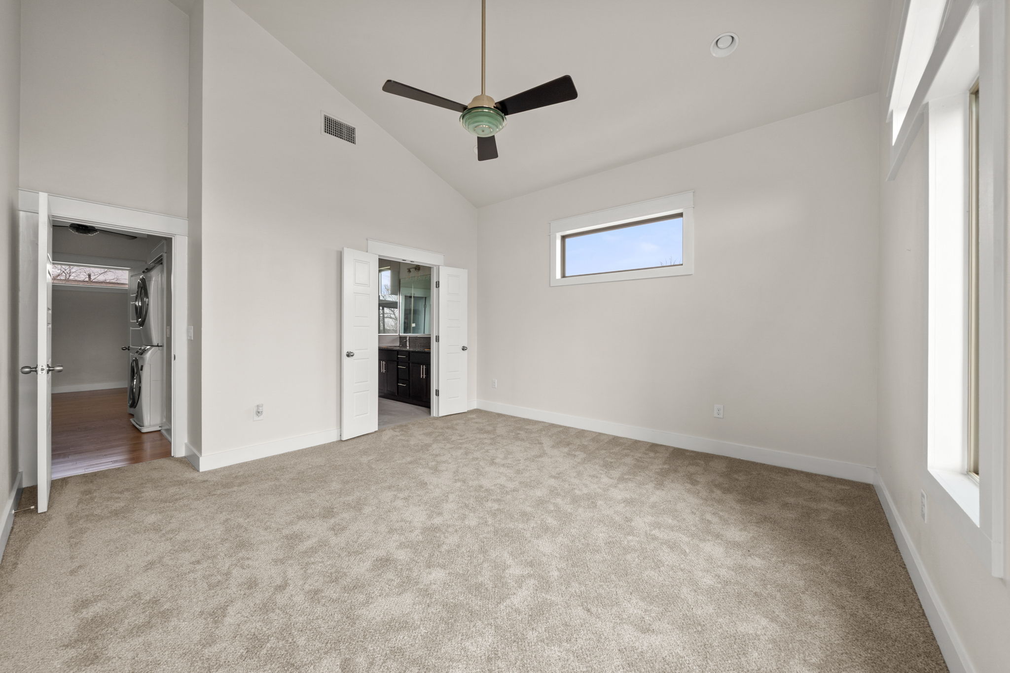 1160 Nickols Avenue, Unit A Austin, TX 78721 - Photo 25 of 40 Unfurnished bedroom featuring high vaulted ceiling, estacked washer and dryer, light colored carpet, ensuite bath, and ceiling fan