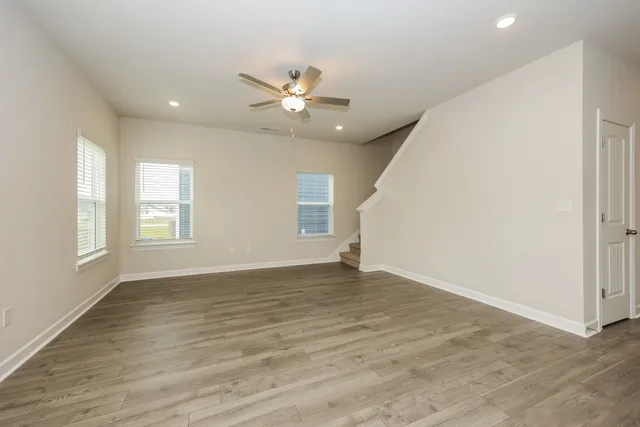 an empty room with wooden floor fan and windows
