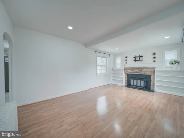 a view of an empty room with wooden floor fireplace and a window