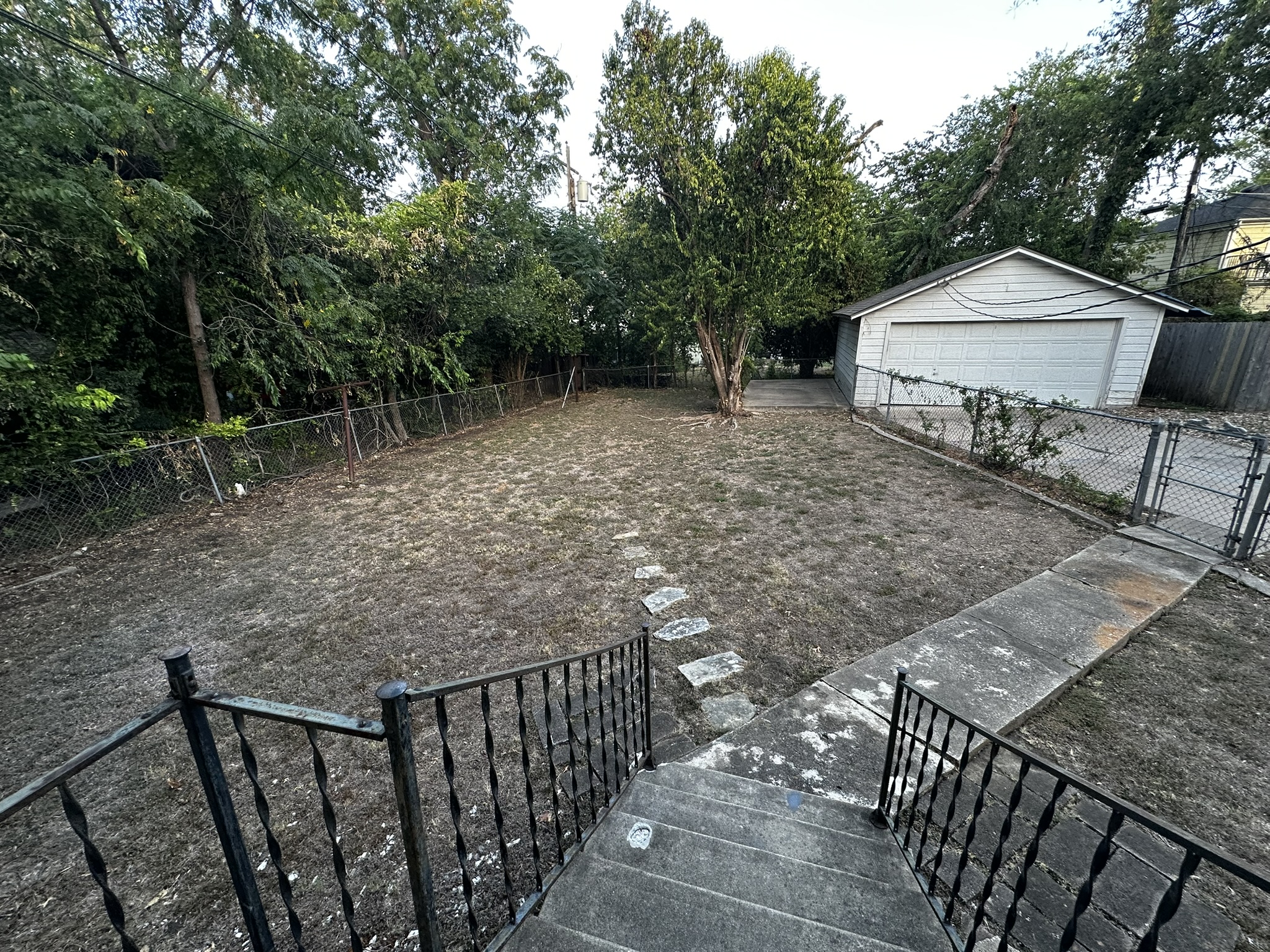 3903 Ridgelea Drive Austin, TX 78731 - Photo 15 of 17 Mature trees line a fenced backyard with concrete steps leading down to the lawn.