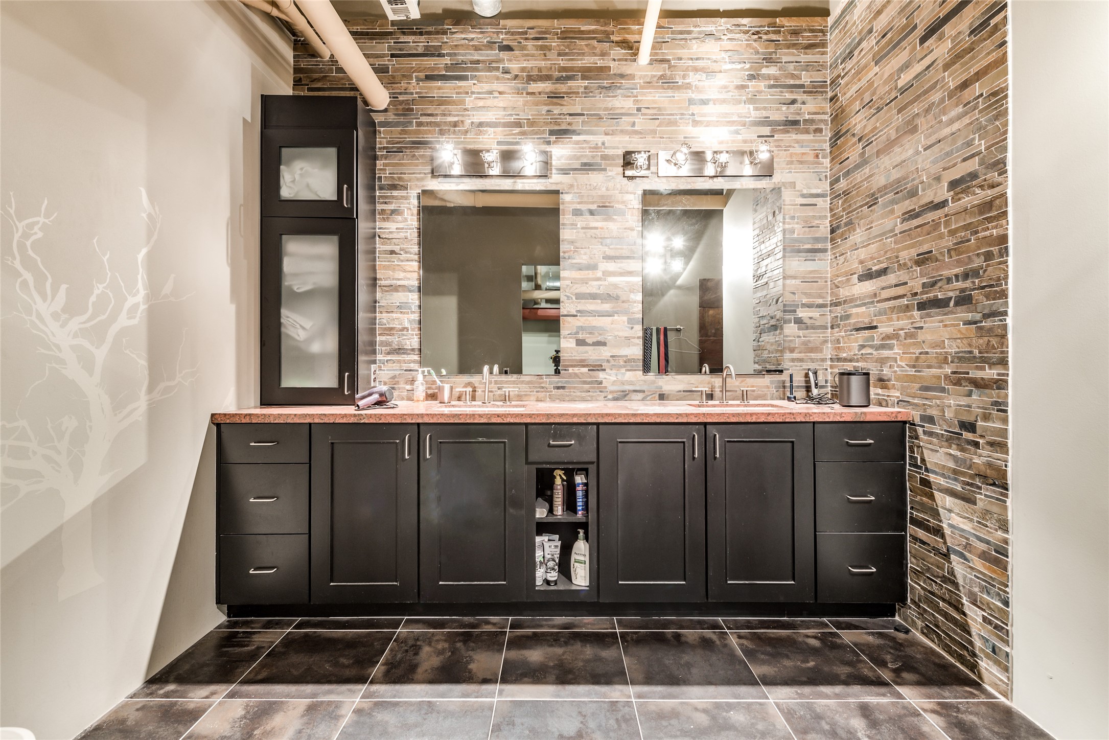 705 Main Street, Unit 215 Houston, TX 77002 - Photo 24 of 36 This modern primary bathroom features a double vanity with dark cabinetry and a sleek stone-tiled wall.