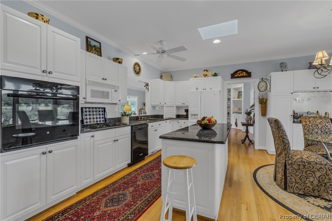 181 Duckbill Road White Stone, VA 22578 - Photo 24 of 50 Kitchen with black appliances, a skylight, dark stone countertops, white cabinets, ornamental molding, backsplash, light hardwood floors, and ceiling fan