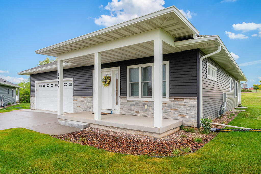 Front exterior of W4936 Battlestone Station Road – front porch, 2-car garage. Vinyl siding with stone.