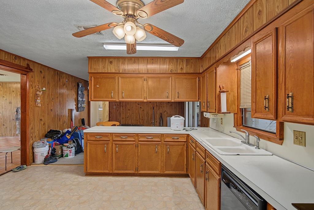 2604 Rosedale Place Bossier City, LA 71111 - Photo 12 of 26 Kitchen featuring wood-paneled walls, wood cabinetry, white countertops, a double basin sink, and ceiling fan with integrated lighting