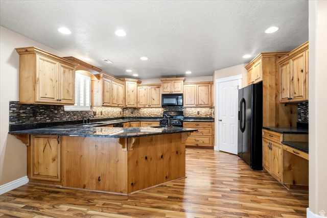 1089 West 2325th Street North Layton, UT 84041 - Photo 9 of 40 Spacious kitchen featuring extensive wood cabinetry, dark countertops, a large central island, black appliances, and wood-finish flooring