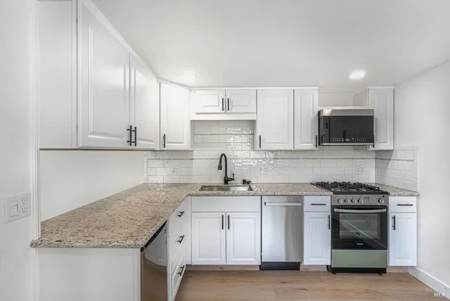 a kitchen with granite countertop a sink stainless steel appliances and white cabinets