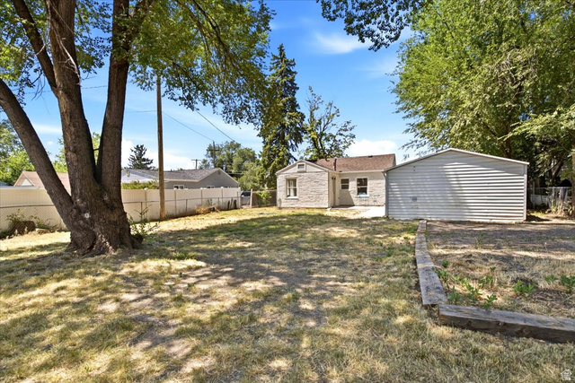 307 Flint Street Layton, UT 84041 - Photo 13 of 13 Expansive backyard featuring a mature tree, a detached garage with horizontal siding, and a stone-clad exterior on the main residence