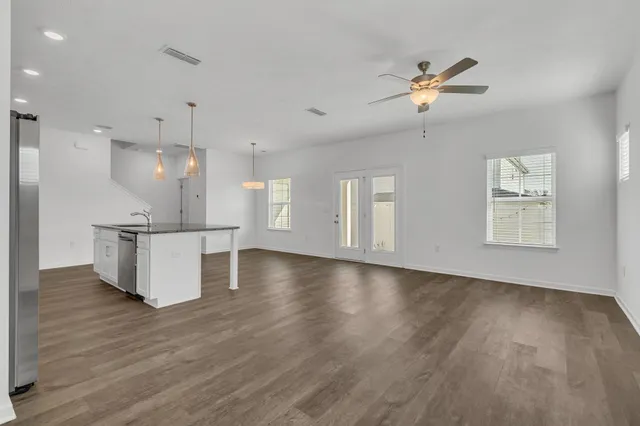 a view of an empty room with wooden floor and a kitchen