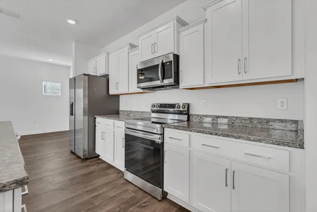a kitchen with stainless steel appliances granite countertop a refrigerator stove and white cabinets