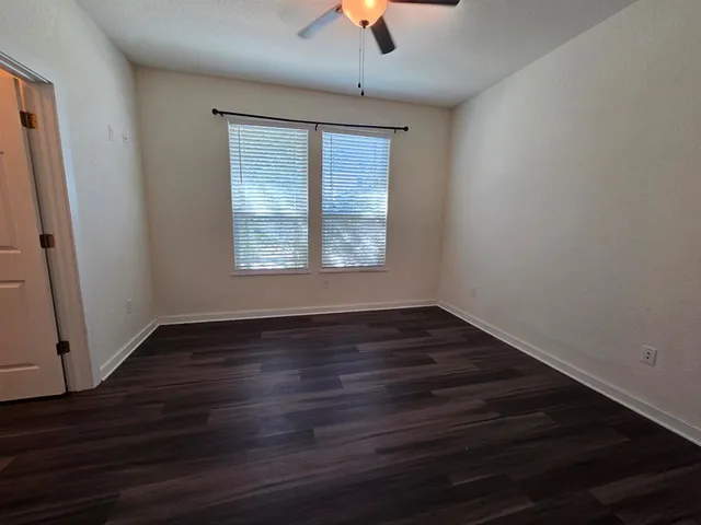 an empty room with wooden floor chandelier fan and windows