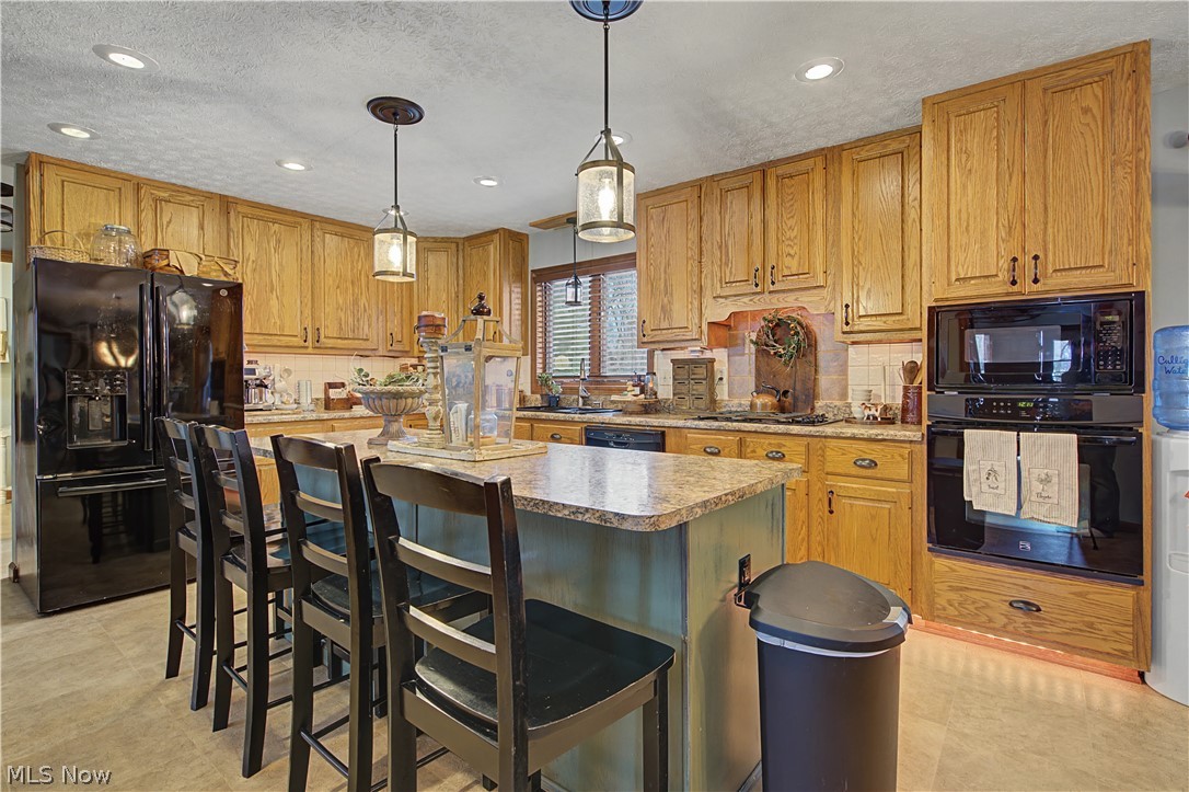 55 Coal Run Road Marietta, OH 45750 - Photo 8 of 30 Kitchen featuring black appliances, a kitchen breakfast bar, hanging light fixtures, wood finish cabinets, and a textured ceiling