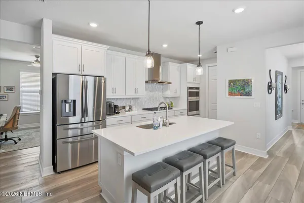 a kitchen with stainless steel appliances a refrigerator a sink a stove a kitchen island and chairs with wooden floor