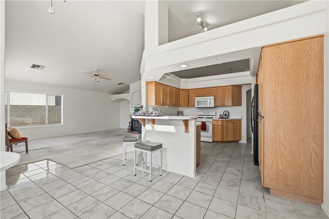 2853 Winchester Road Bullhead City, AZ 86442 - Photo 18 of 40 Kitchen featuring wood-finish cabinetry, white appliances, and a breakfast bar with a solid surface countertop